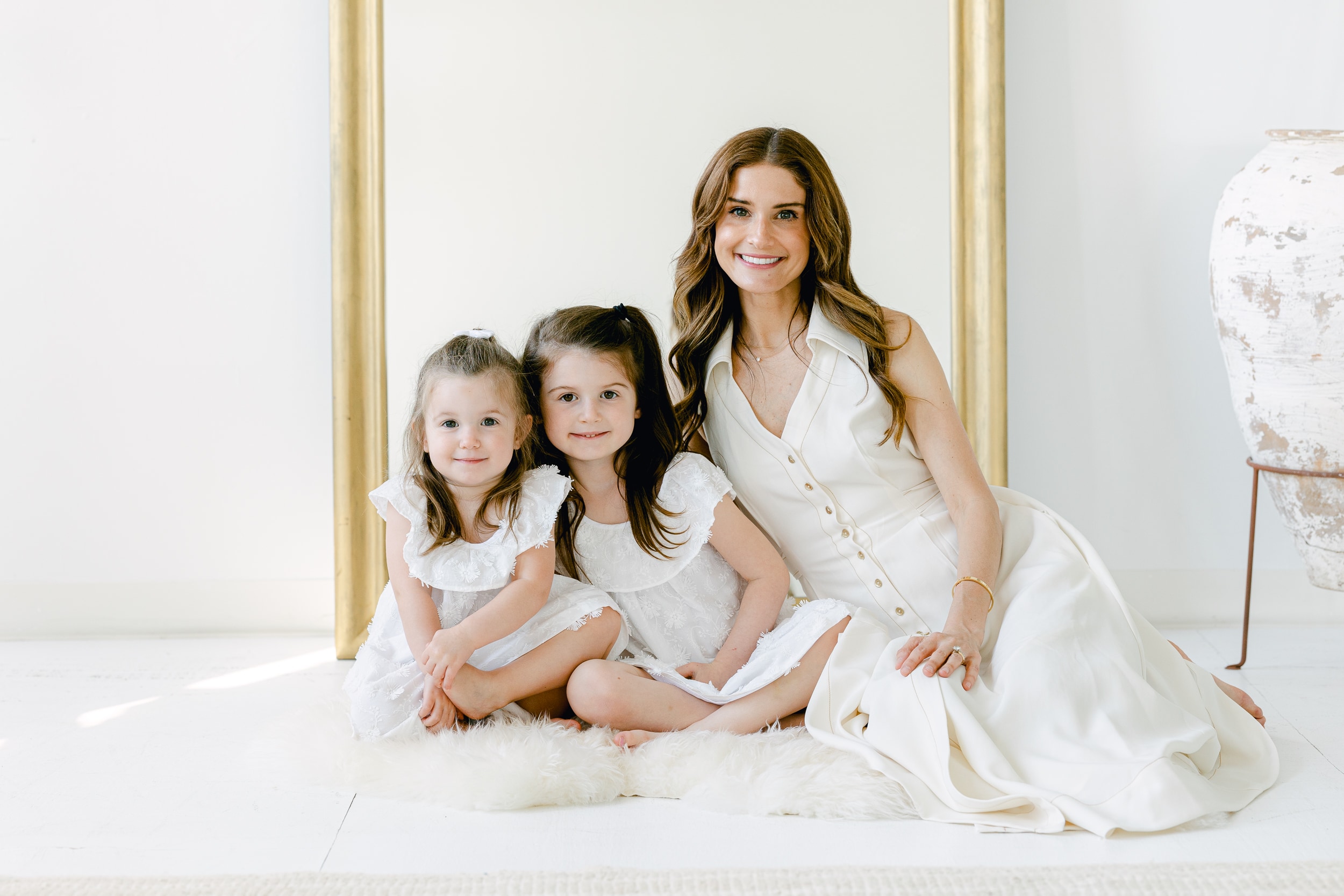 Mom sitting with daughters in front of mirror, in white dresses