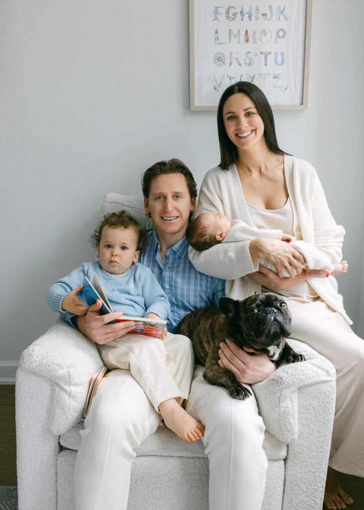 New York family of four plus dog, sitting together and reading in a white armchair.