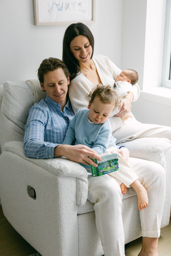 New York family of four in white and blue read together in a large white armchair.