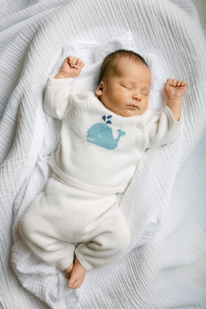 Newborn baby in a white knit set with blue whale and button details on sweater from Pinwheels Kids.