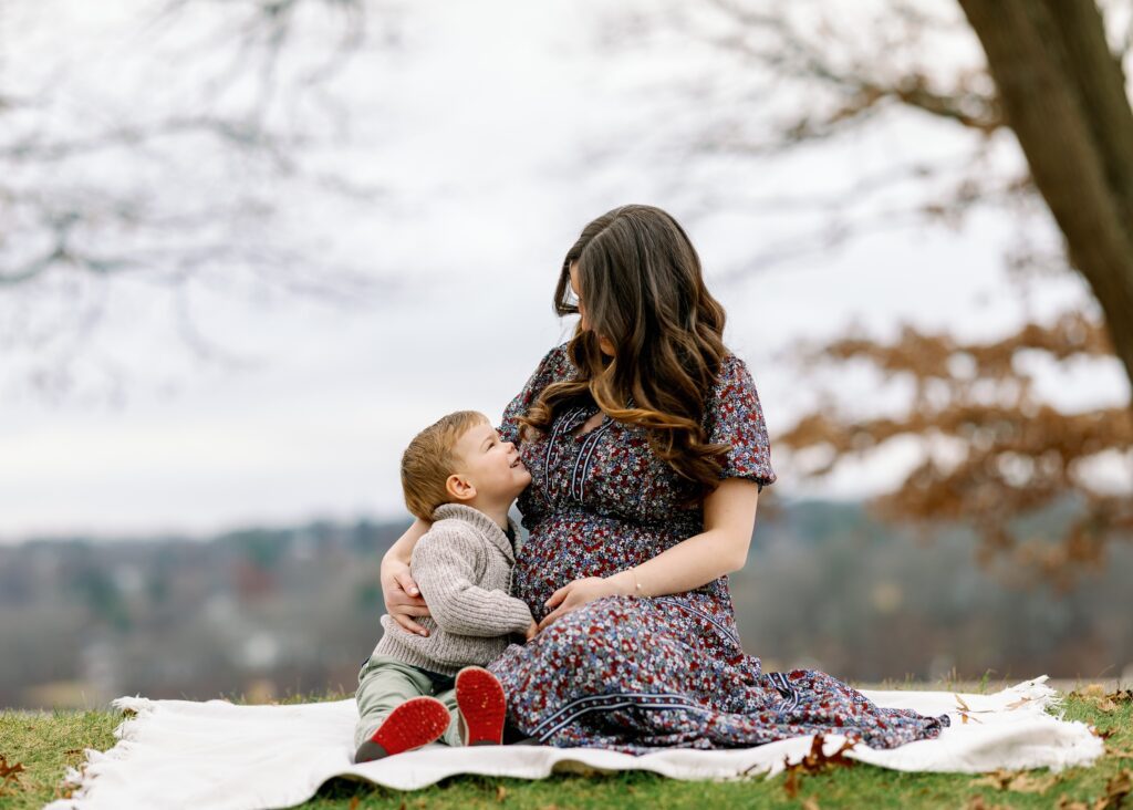 Mom and toddler boy sitting on blanket in the park, looking lovingly into each other's eyes. 