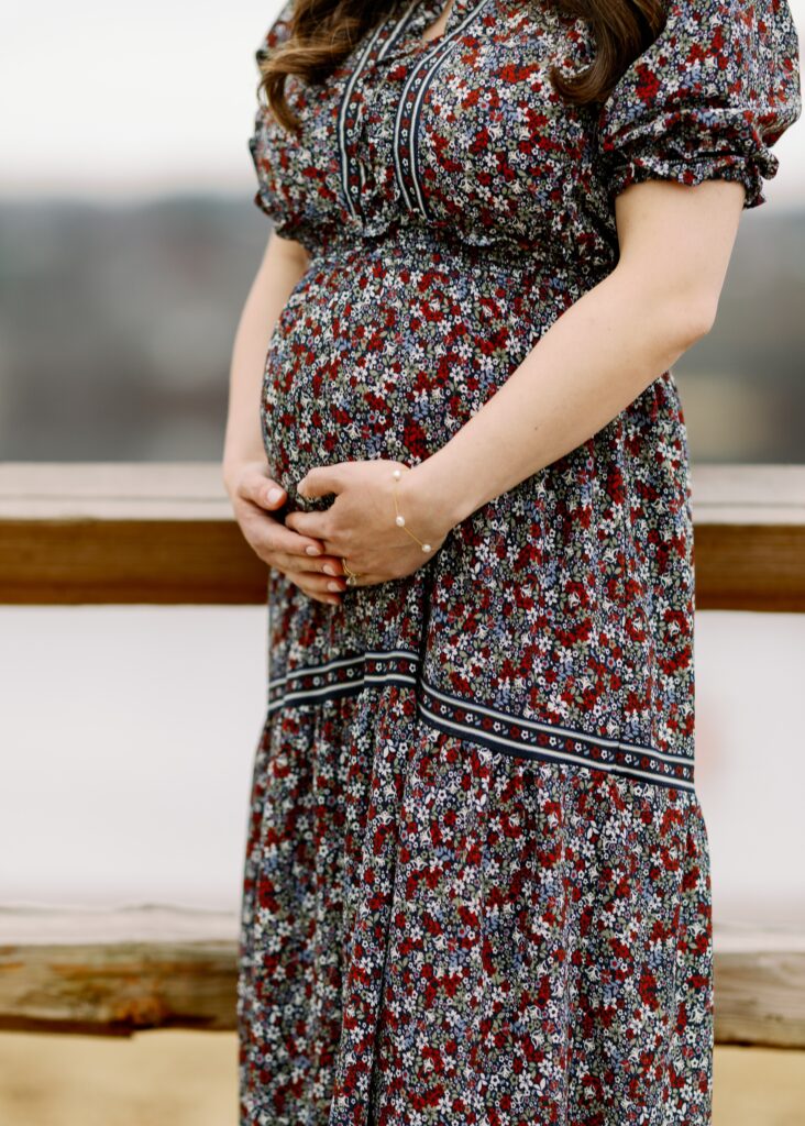Mom in long floral dress cupping her pregnant belly with her hands. 