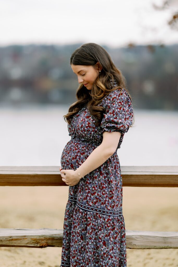 Brunette mom in long floral dress holding pregnant belly and lovingly gazing down at it. 