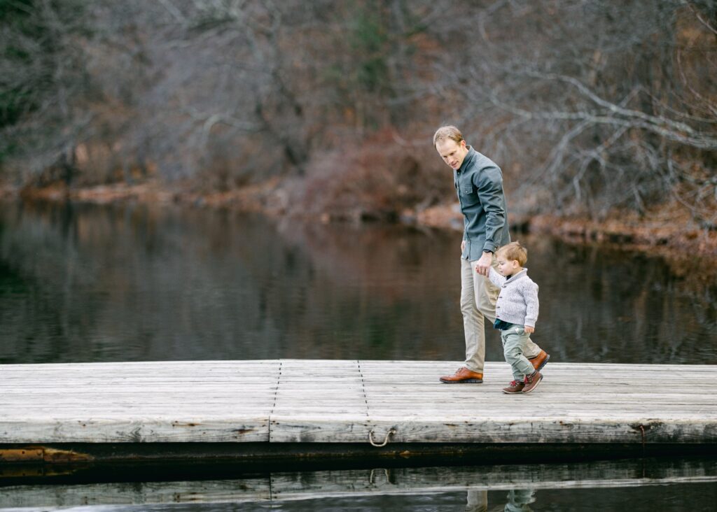 Dad and toddler boy holding hands and walking on a dock. 