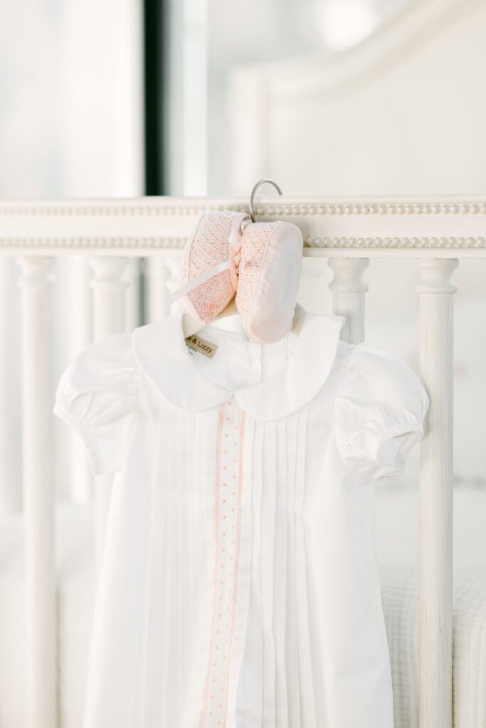 White baby dress with light pink booties hanging off crib.