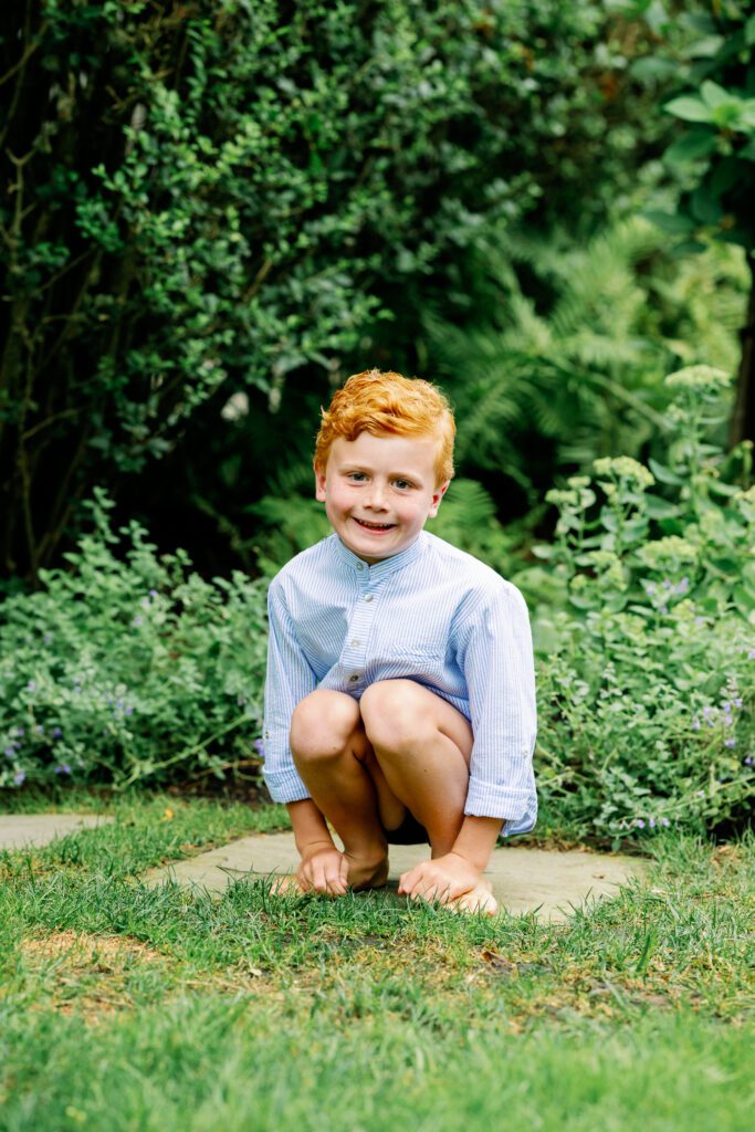 Young red-headed boy squats in a stepping stone in backyard.