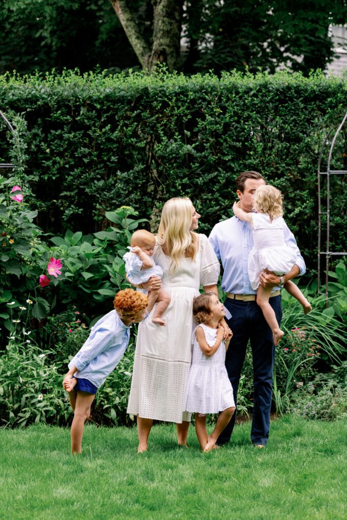 Family of six in their green backyard, wearing white and blue, looking up at dad.