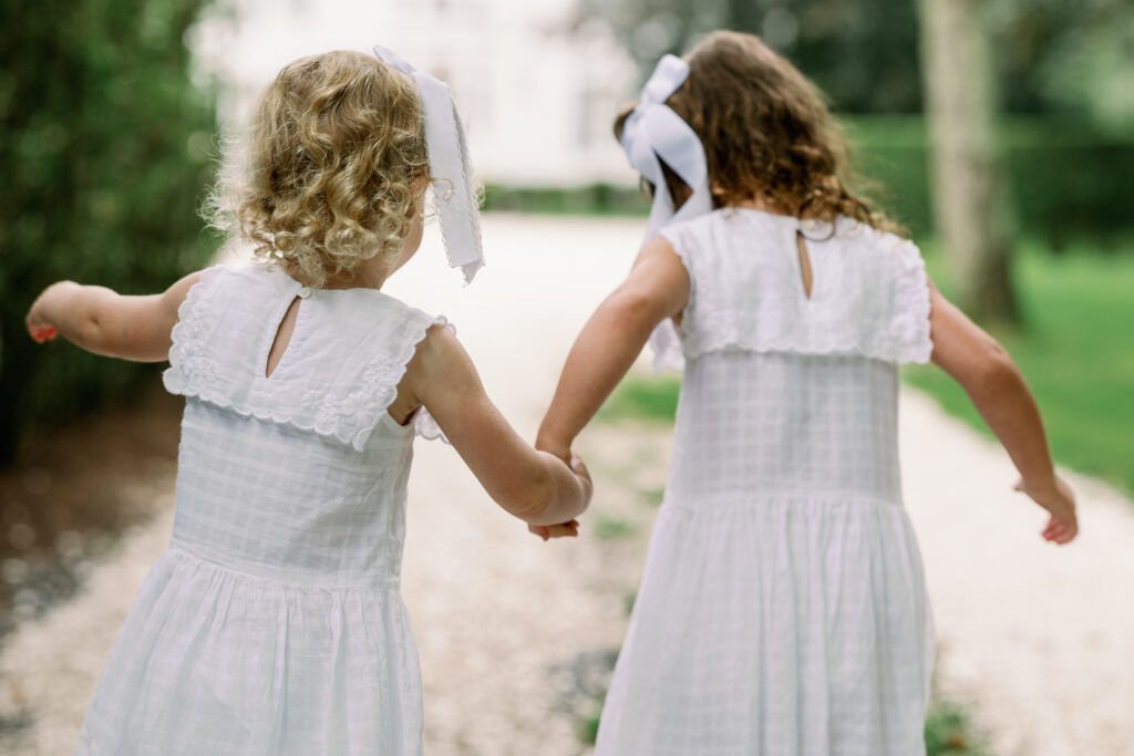 Two sisters in white dresses hold hands and run down the shelled driveway of their Nantucket vacation home.