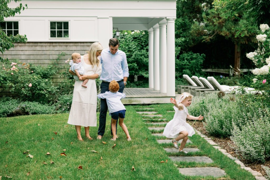 Mom, dad, and three children, all in white and blue, play in the garden.