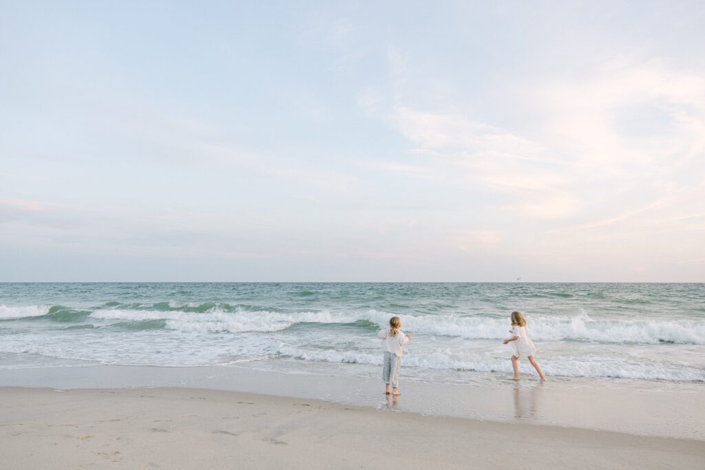 Distance shot of two blonde sisters playing in the ocean. 