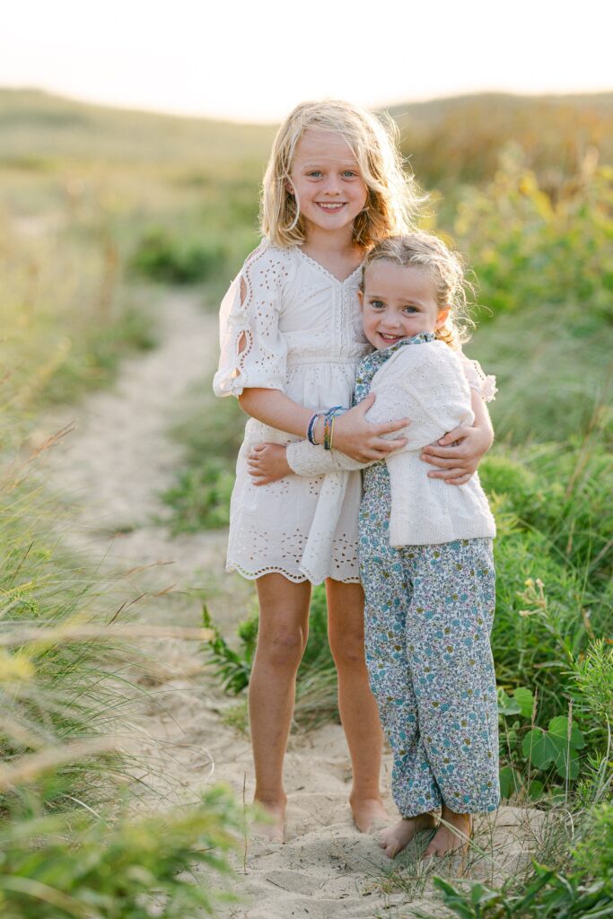 Two blond sister's hugging one another and smiling at the camera. 