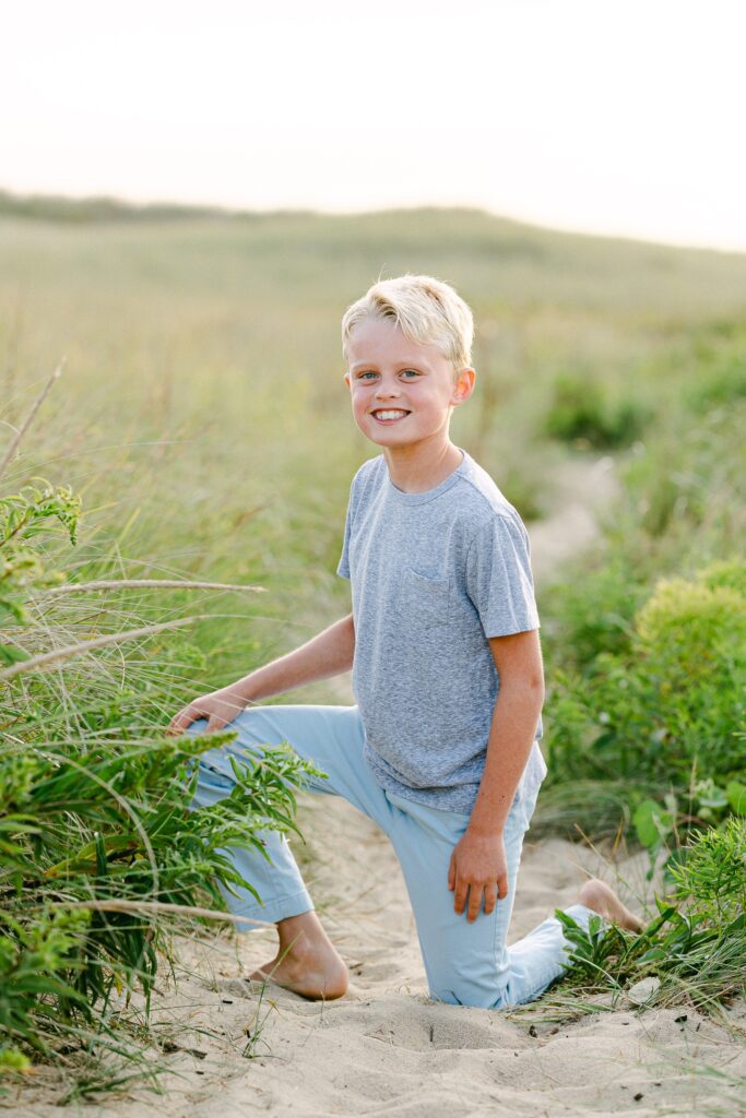 Close-up of oldest brother on one knee in the sand dunes smiling at the camera. 