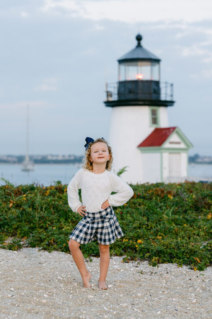 Daughter with big navy bow is striking a pose with hands on her hips in front of Brandt Point Lighthouse. 