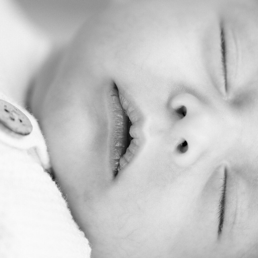 Close-up shot of baby newborn's sleeping face with closed eyes and slightly parted lips. 