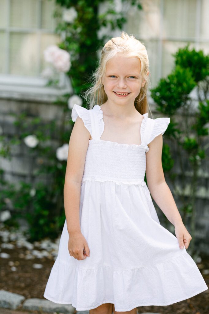 Blond girl is smiling and holding out the skirt of her dress with one hand. 