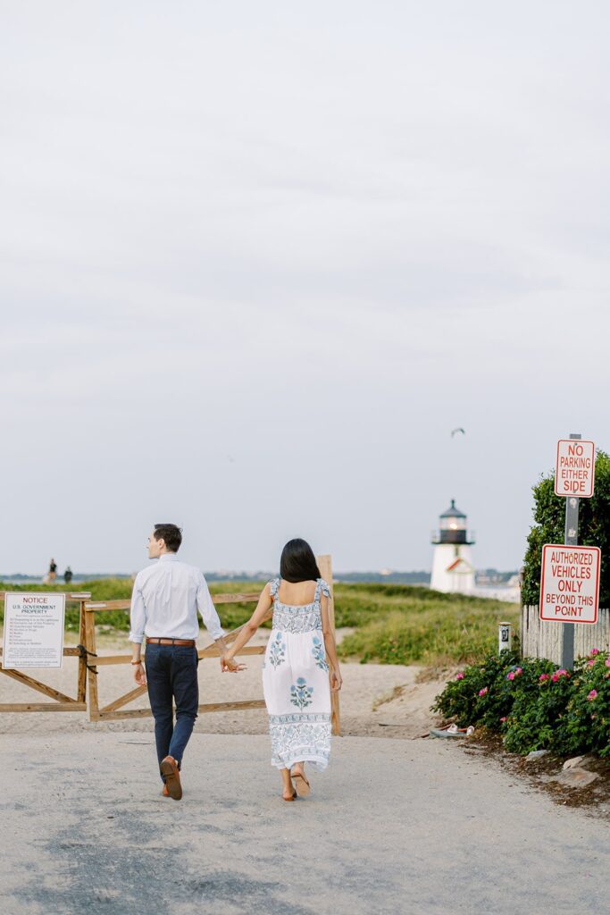 Man in a light blue button down and dark slacks is walking hand-in-hand with a brunette woman in a white, blue, and green floral block-print sundress. 