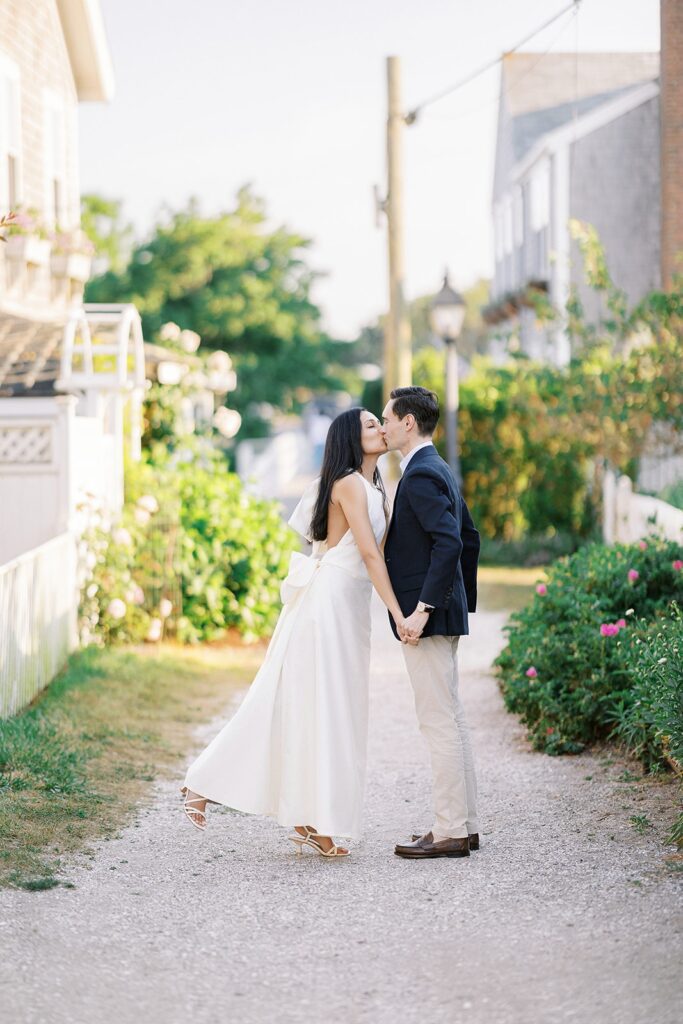 Brunette woman in ivory dress is kissing a man in a navy sport jacket and khaki pants. They are holding hands. 