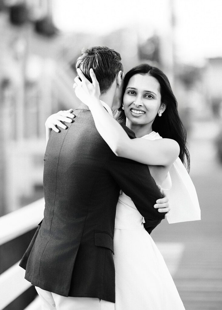 A man and woman are in a tender embrace - his arms are round her waist and she has a big smile on her face with one arm around his shoulder and the other cupping the back of his head. 