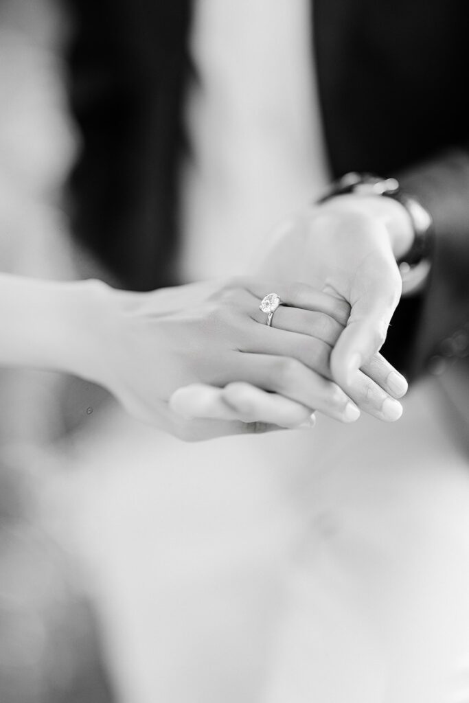 A man's hand holding a women's hand showing off a large single-stone round diamond engagement ring. 