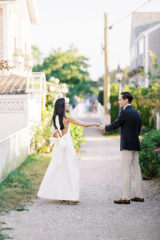 Brunette woman in ivory dress is extending her arm and holding the hand of a man in a navy sport jacket and khaki pants. They are smiling at each other and look to be in a mid-dance twirl. 