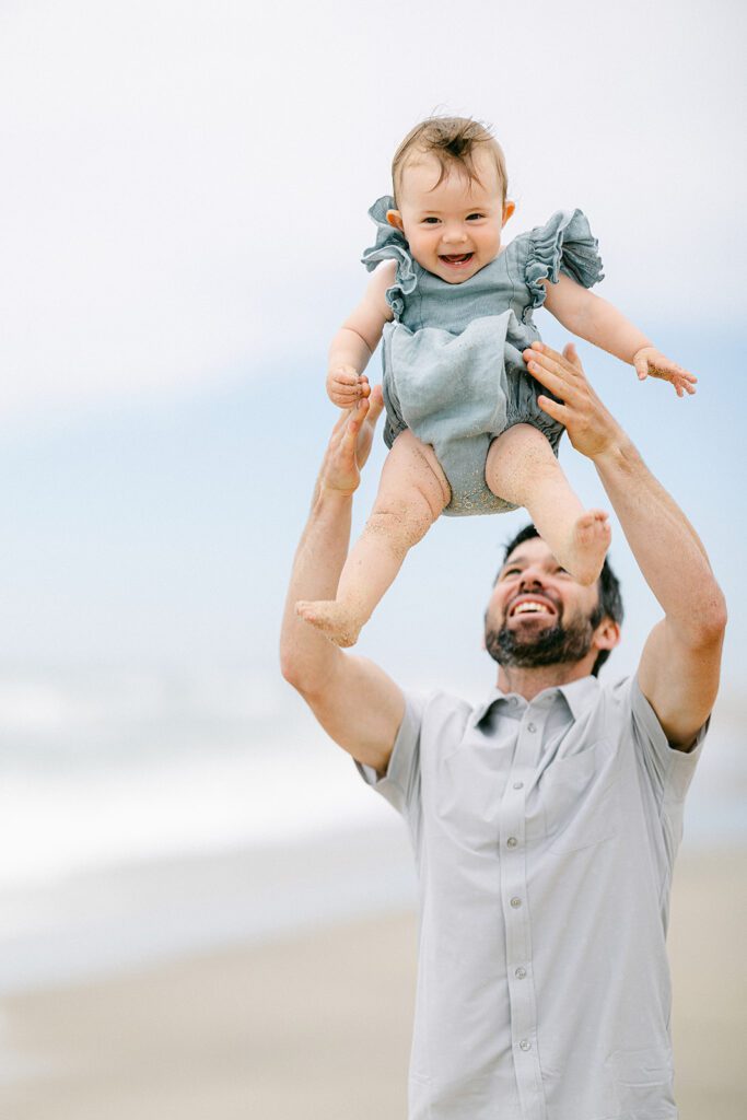 Bearded dad is tossing his smiling brunette baby girl into the air.