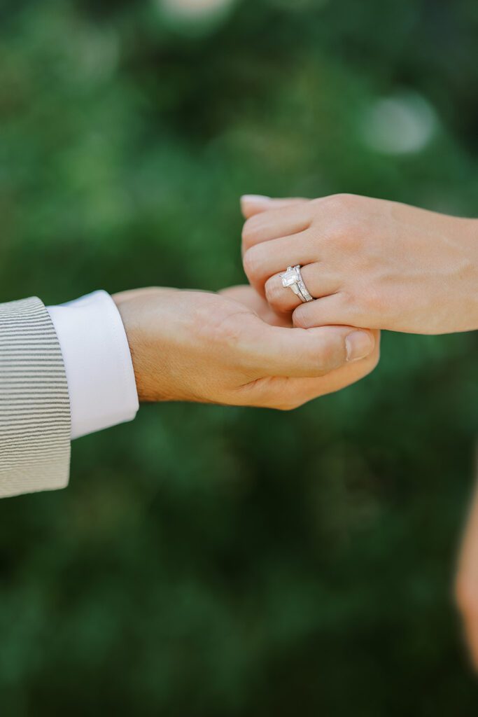 A man's hand it gripping the fingers of a female's hand with her engagement and wedding ring of visible. 