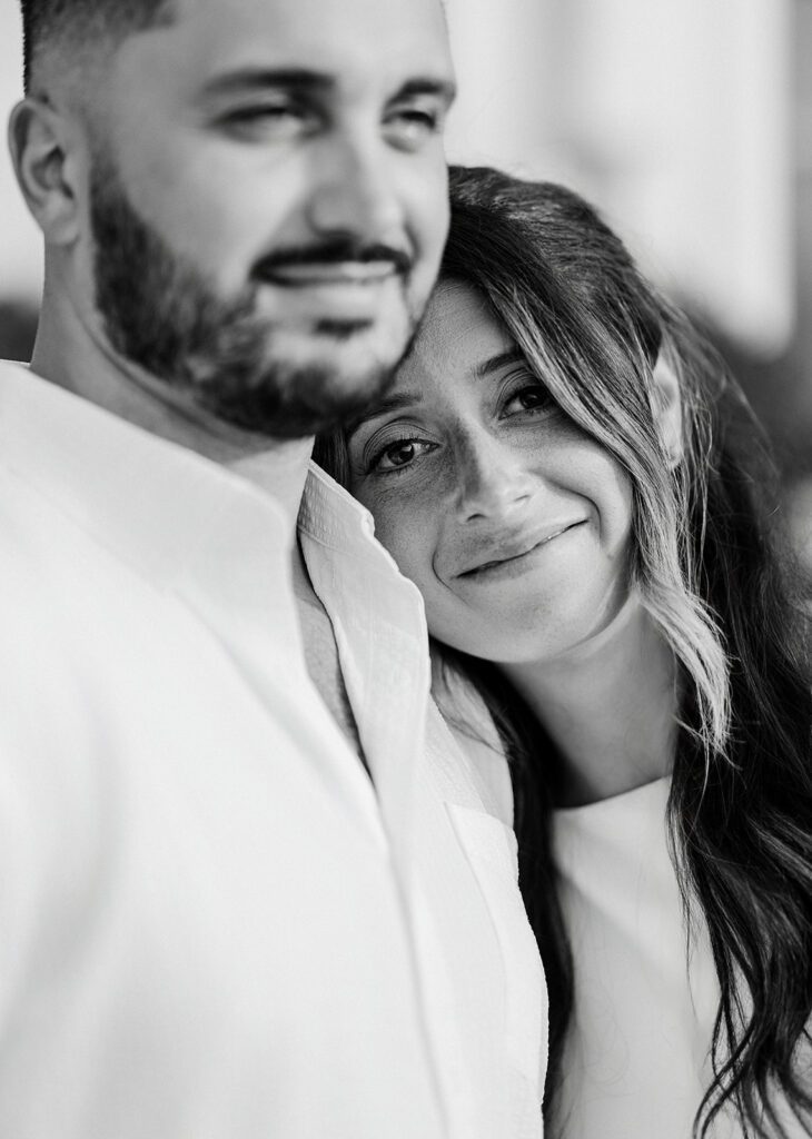 A woman with long hair is resting her head on the chest of a bearded man - they are both smiling. 