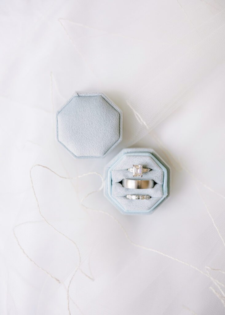 An engagement ring and wedding rings are cushioned inside a pale blue, octagon-shaped ring box on display. 