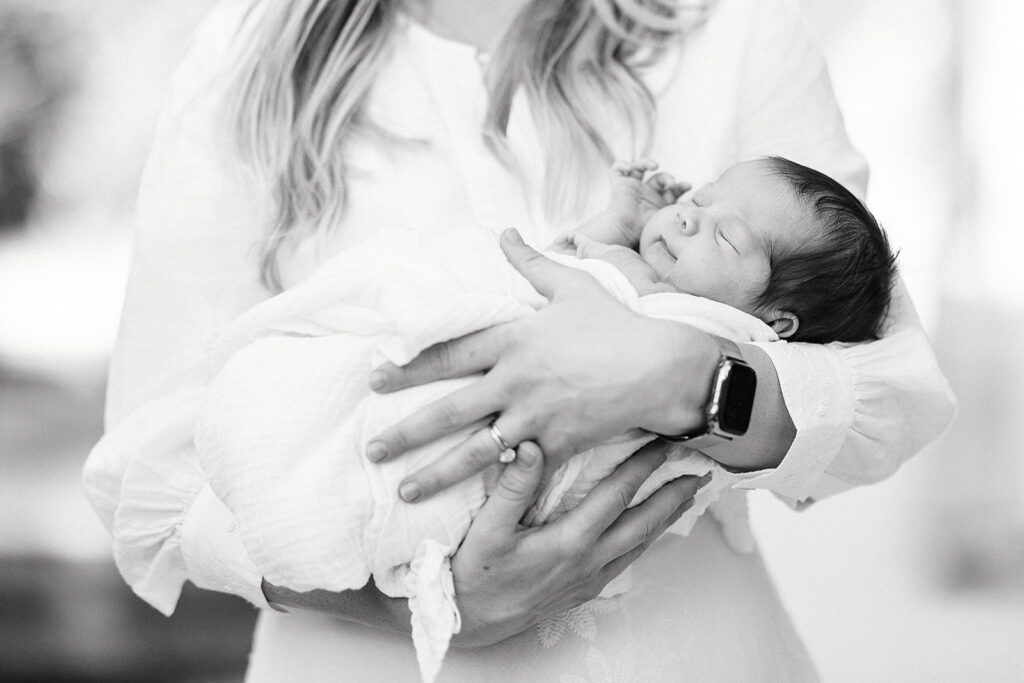 Dark-haired newborn baby is swaddled and snuggled up while sleeping in mom's arms 