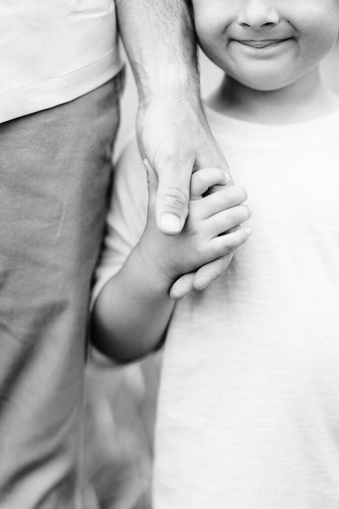 Black and white closeup image of a boy and his father holding hands.