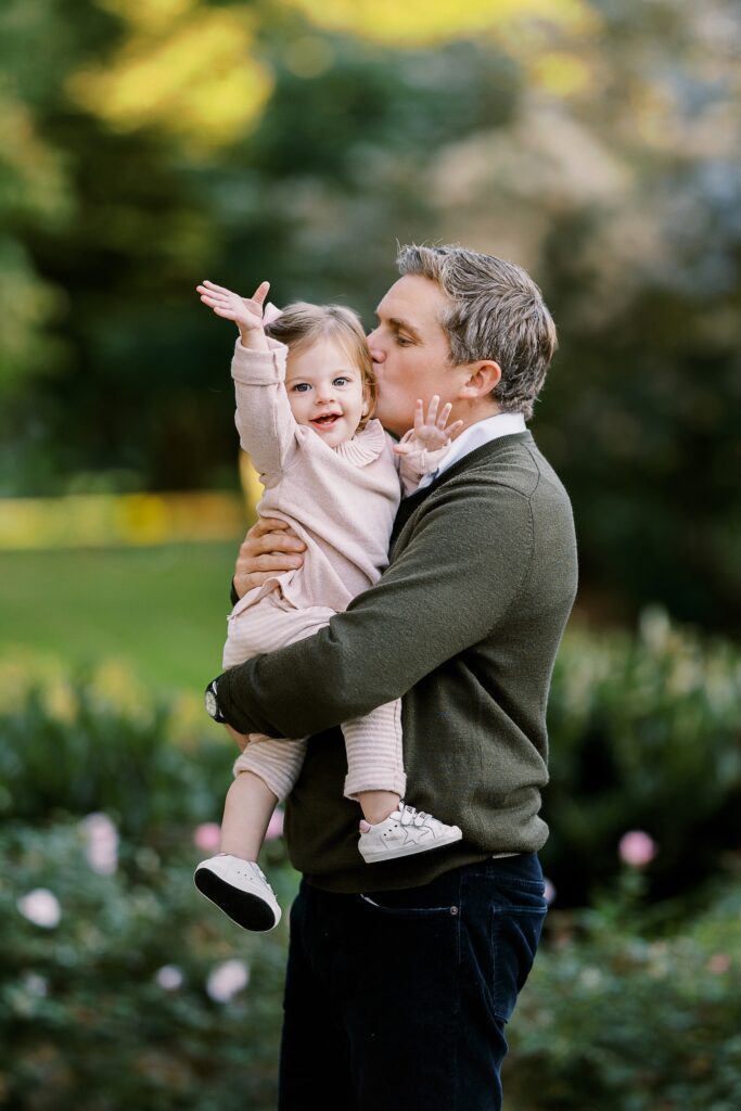 Profile of father holding his toddler daughter, who is smiling and waving at the camera.