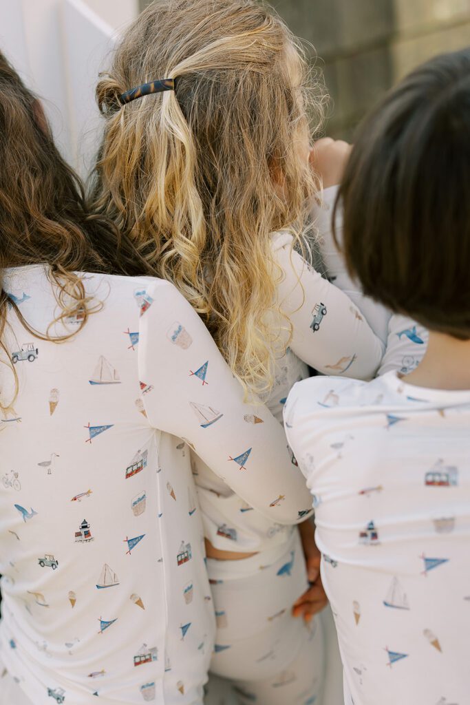 Three siblings are seen from behind standing scrunched together wearing pajamas with hand-drawn sketches featuring Nantucket imagery.