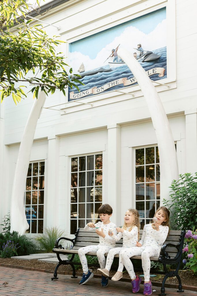 Three kids in pajamas eating ice cream on a bench outside the Nantucket whaling museum.