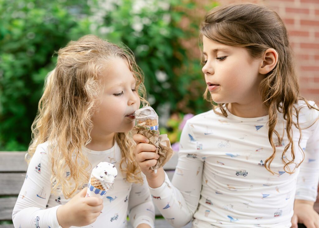 Two sisters sit on a bench and share ice cream cones - both are wearing pajamas with hand-drawn sketches featuring Nantucket imagery.