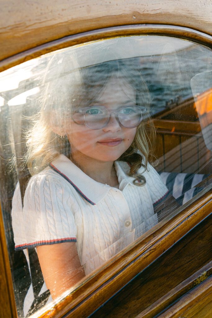 A young girl is looking at the window from inside the wood-paneled cabin of The Blue Peter Yacht sailboat on Nantucket. 