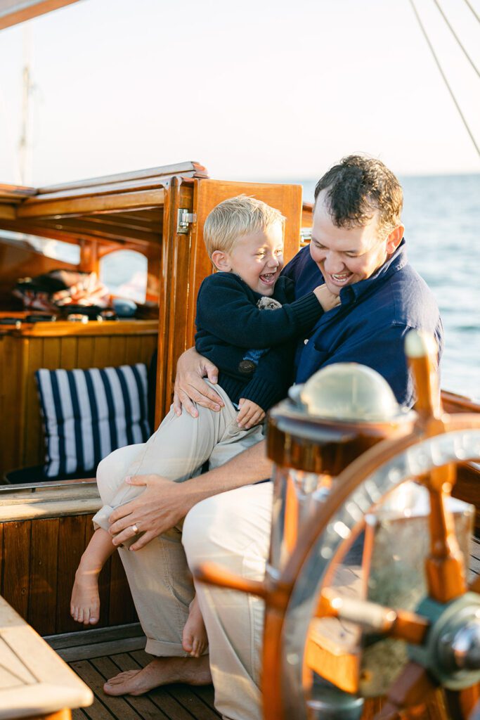 A father and son are laughing with each other while sitting on the deck of The Blue Peter Yacht sailboat on Nantucket.