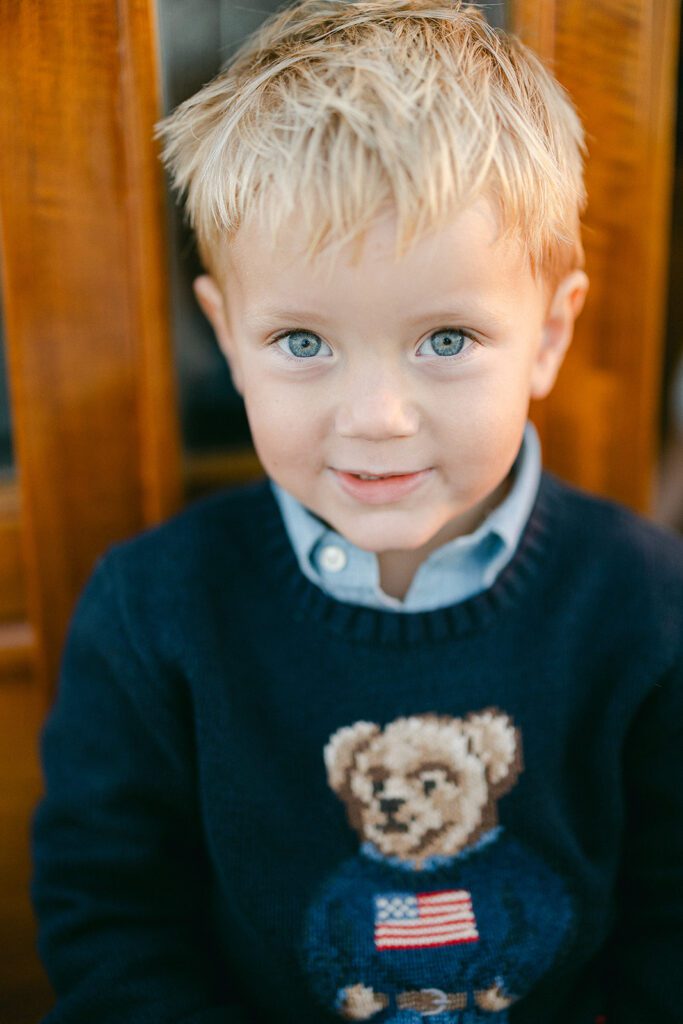 A young boy is smiling and standing in front of the wood cabin of The Blue Peter Yacht sailboat on Nantucket. 