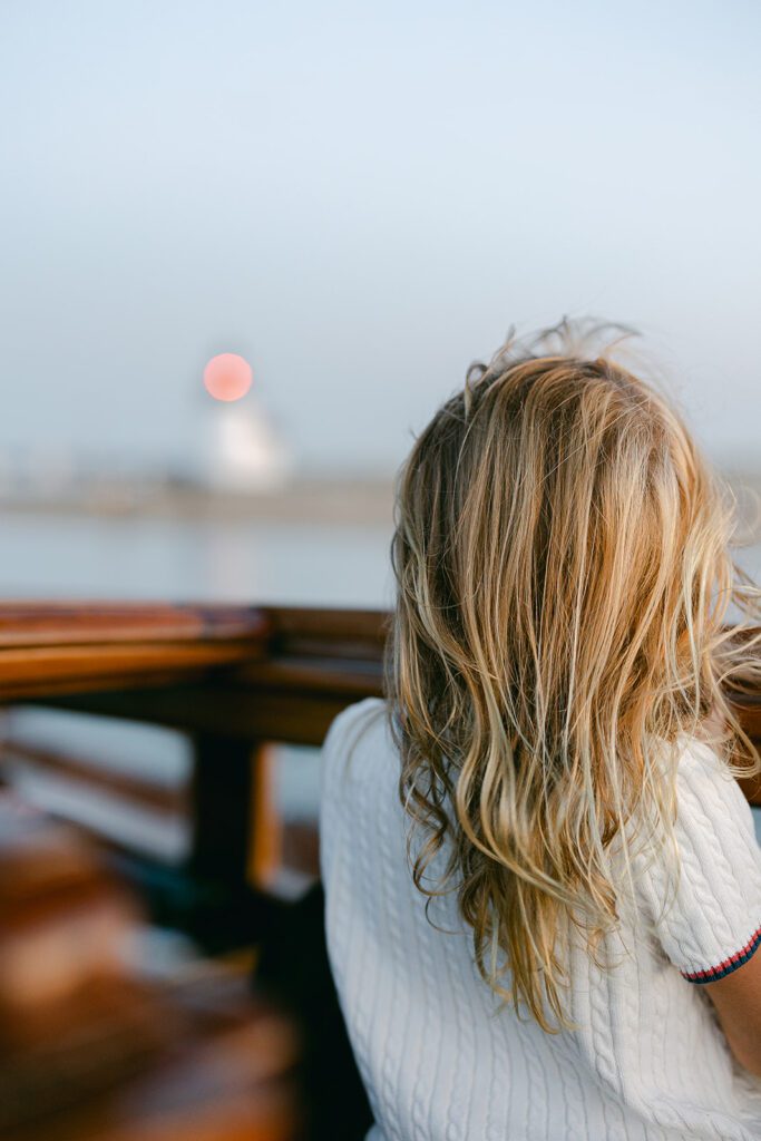 A young girl is looking at the sunset over the railing of The Blue Peter Yacht sailboat on Nantucket. 