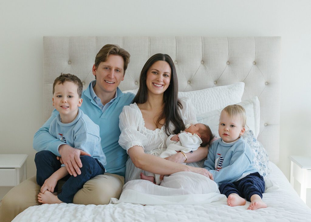 A family of five sit cuddled up on the bright white duvet of their bed, exuding pure happiness in their smiling faces in the Connecticut suburbs. 