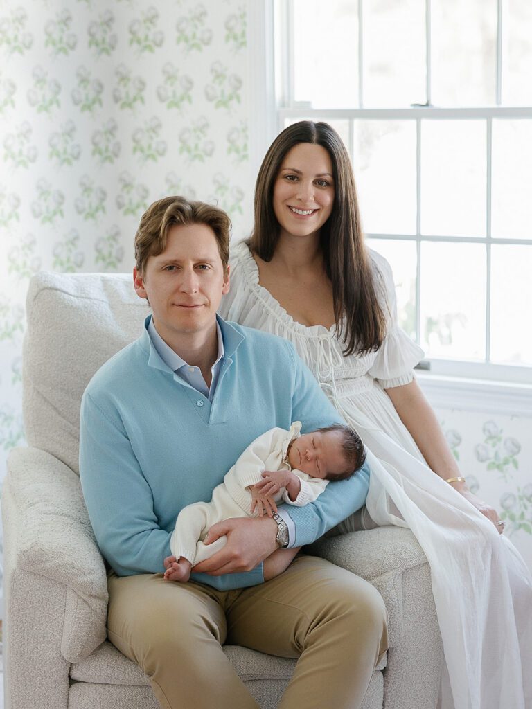 A husband and wife pose with their newborn baby girl while sitting on the rocker in the nursery of their home in the Connecticut suburbs. 