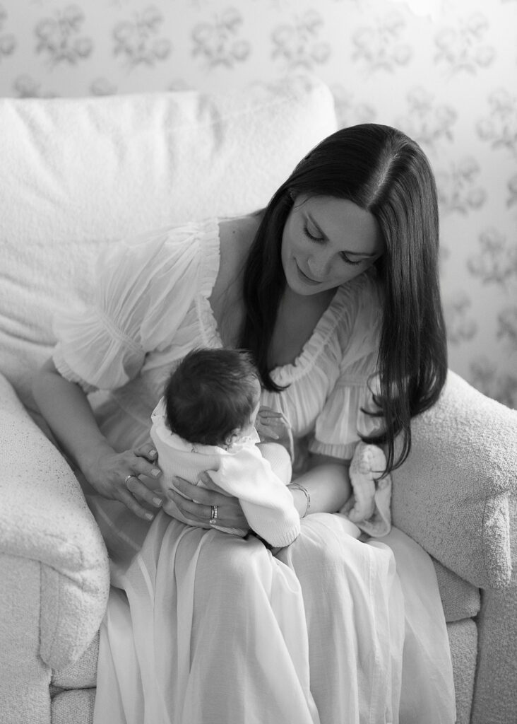 A mother is sitting on a rocker, re-positioning her newborn daughter on her lap at home in the Connecticut suburbs. 