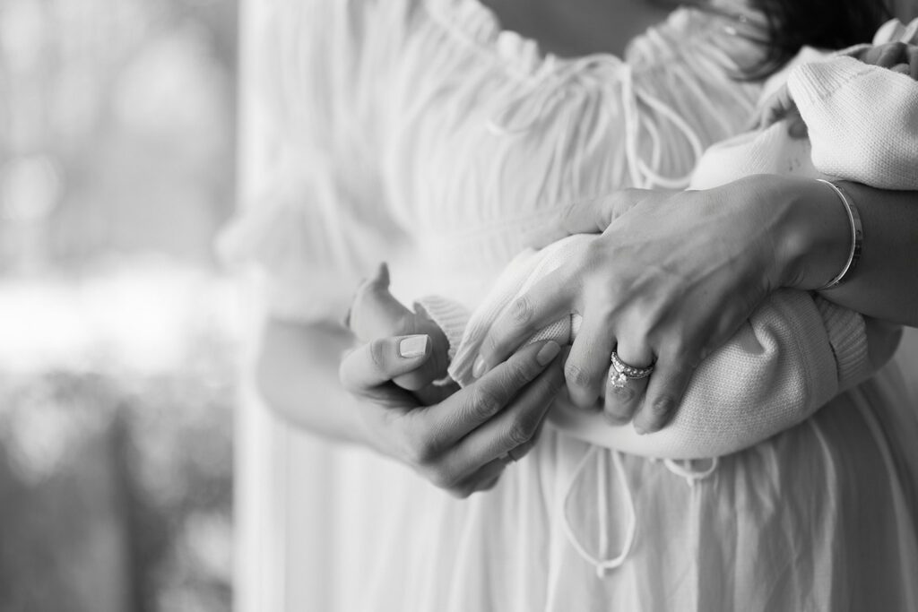 A mother is holding her newborn daughter in the crook of her arm, cupping her tiny feet with her free hand, in her home in the Connecticut suburbs. 