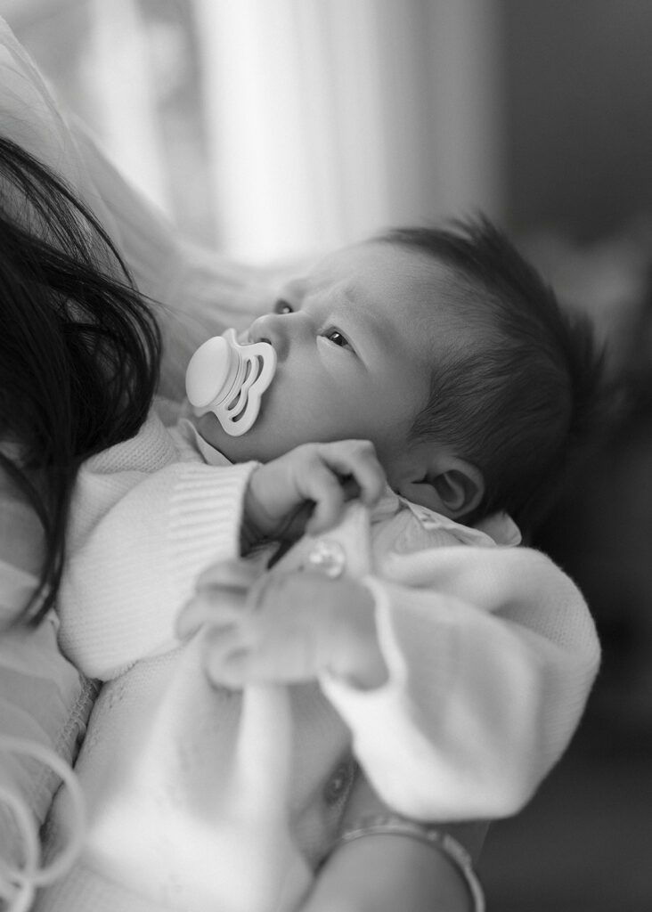 A newborn baby is being soothed in the crook of her mother's arm with a pacifier in her mouth and her eyes on her momma at home in the Connecticut suburbs. 