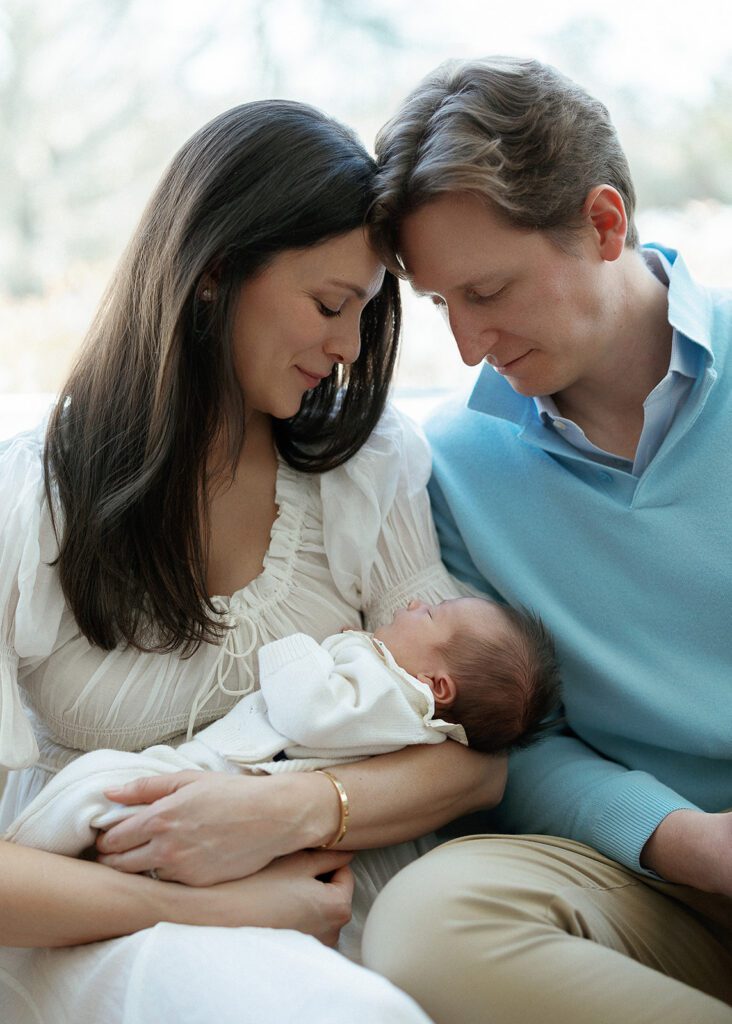 A husband and wife cuddle their newborn baby closely, staring at her in wonder, in their home in the Connecticut suburbs. 