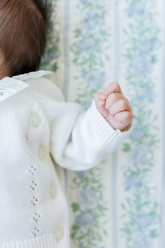 A newborn baby girl's hand is clenched in a fist as she lays on a floral sheet in the nursery of her home in the suburbs of Connecticut. 